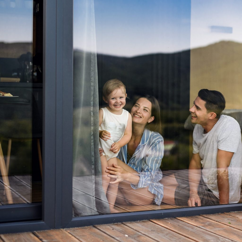 Young family with small daughter indoors, weekend away in container house in countryside. Shot through glass.